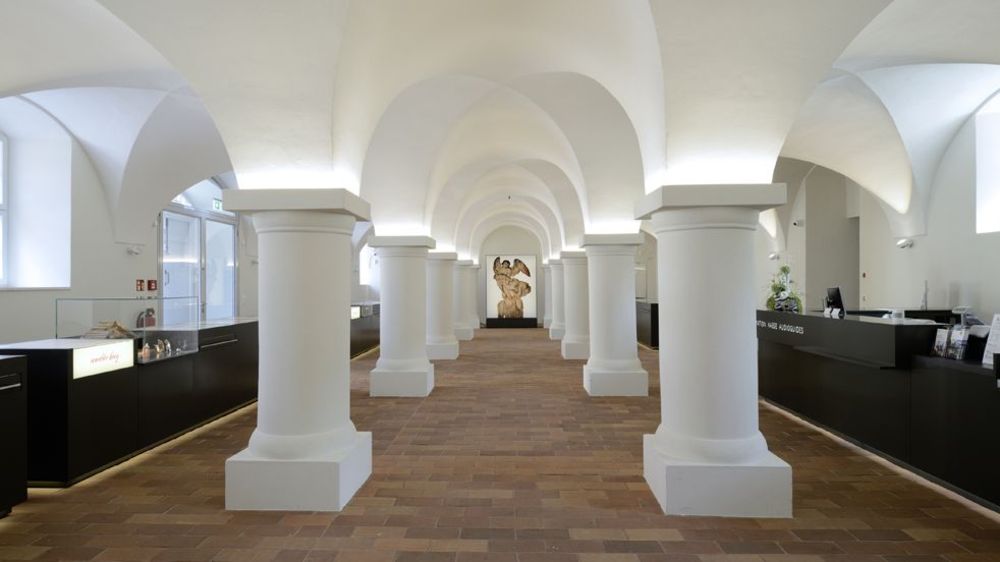 Innenansicht. Blick in den hellen Eingangsbereich. Der Raum ist dreischiffig mit dicken Säulen und einer gewölbten Decke.