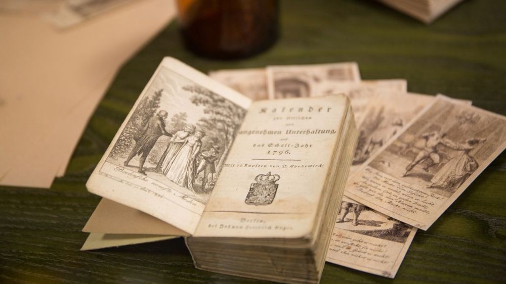 Innenansicht. Ein aufgeschlagenes Buch von 1796 liegt auf einem Tisch mit grüner Platte.